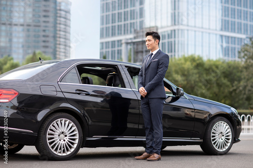 Young Chinese chauffeur standing next to a car photo