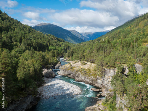 View on azure Rauma river canyon at Romsdalen valley with snow capped peaks of mountains, rocks and green forest. Blue sky white clouds background. Norway summer landscape scenery