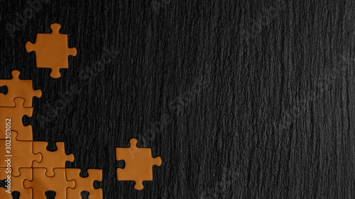 Orange puzzle in the corner of the image on a black natural stone background of slate. A frame with an empty space for your description.