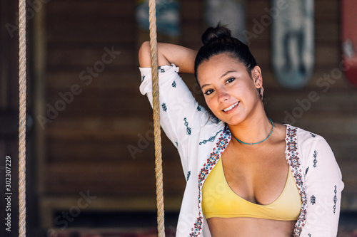 Tanned happy woman in casual wear sitting on swings and looking at camera over wooden wall in Costa Rica photo