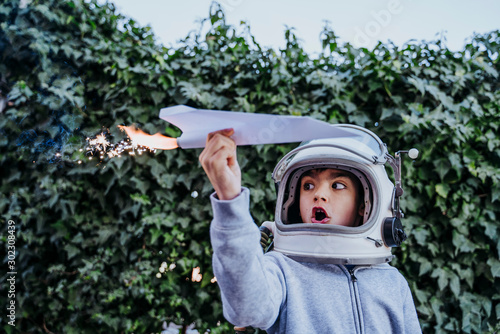 Excited boy in astronaut helmet playing with paper plane with petard in garden photo