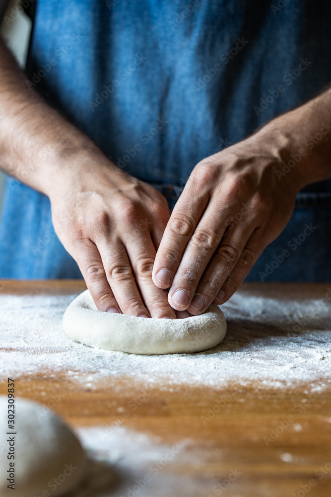 Unrecognizable male in apron flattening soft dough over table with flour while cooking pizza Unrecognizable male in apron flattening soft dough over table with flour while cooking pizza