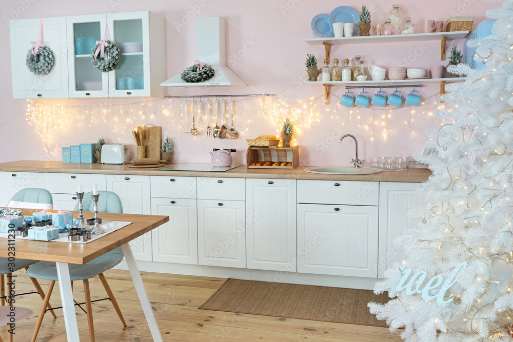 Interior of modern white kitchen and decoration on a Christmas New year eve. Pine tree with wrapped gifts and lights Interior of modern white kitchen and decoration on a Christmas New year eve. Pine tree with wrapped gifts and lights
