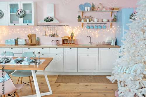 Interior of modern white kitchen with pink walls and decoration on a Christmas New year eve. Pine tree with wrapped gifts and lights