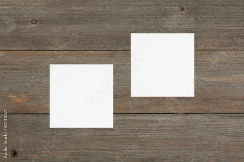 Two empty square white business cards template on wooden background. Flat lay, top view. Uneven, open composition. For branding identity, logo design pitches and marketing.