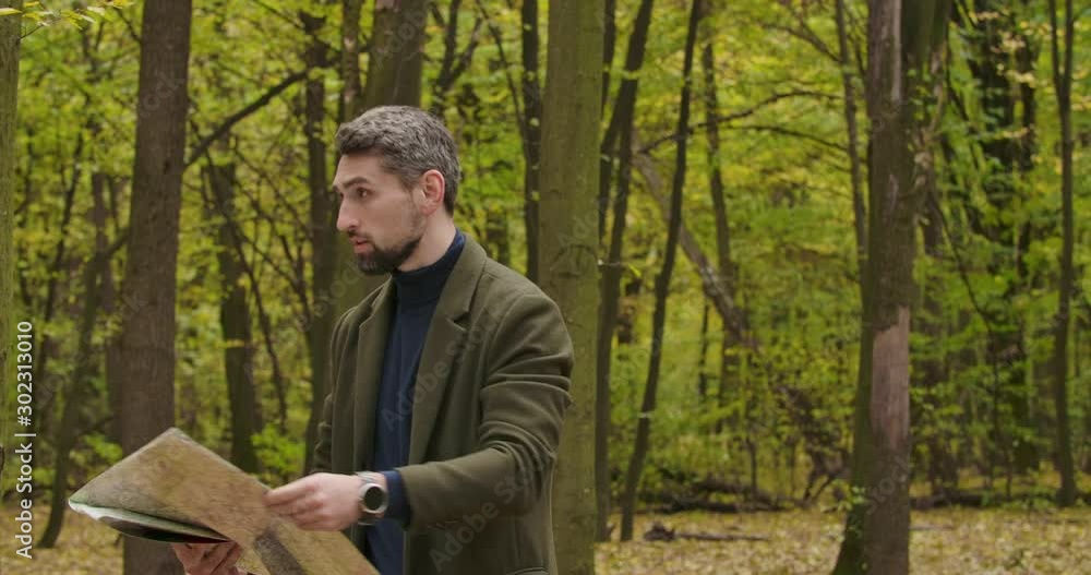 Lost Caucasian tourist standing in the autumn forest between trees and looking at the map and around. Confident man searching the best way to go. Cinema 4k footage ProRes HQ. Lost Caucasian tourist standing in the autumn forest between trees and looking at the map and around. Confident man searching the best way to go. Cinema 4k footage ProRes HQ.