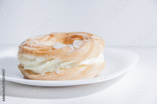 Ring donut cut in the middle and inside whipped cream and on the top almond slices and sugar powder on white plate on bright blue background with space for text