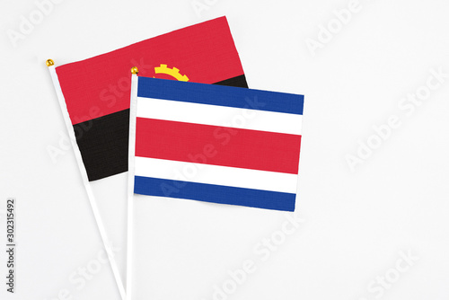 Costa Rica and Angola stick flags on white background. High quality fabric, miniature national flag. Peaceful global concept.White floor for copy space. photo