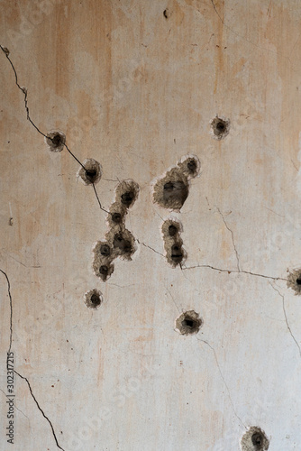 A vertical photo of many bullet holes in a plaster wall. Dirty, cracked interior wall shot repeatedly. Concepts of gun violence, safety and crime 