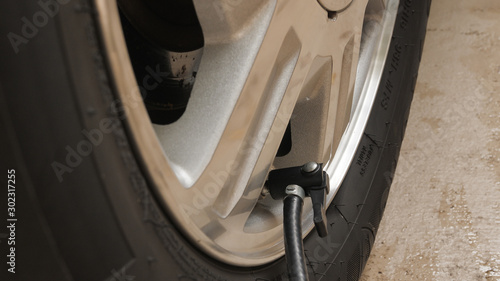 Closeup of air compressor inflation nozzle on valve stem of a car tire. Inflating automotive tire to proper air pressure.