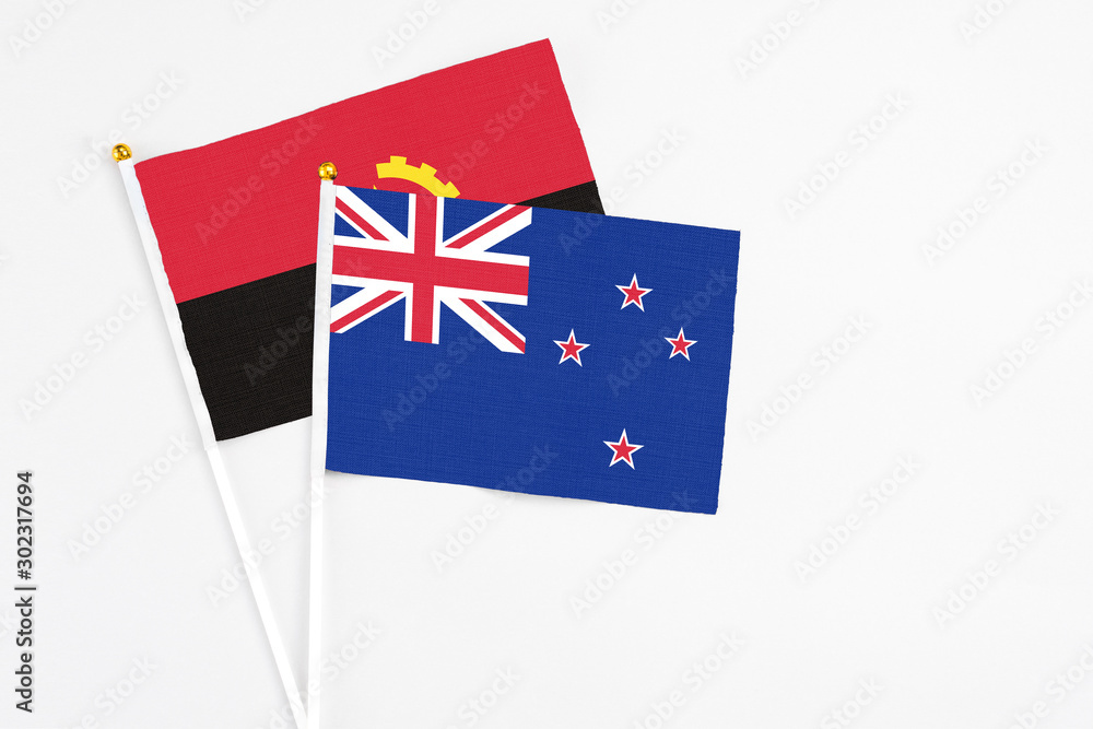 Fototapeta premium New Zealand and Angola stick flags on white background. High quality fabric, miniature national flag. Peaceful global concept.White floor for copy space.