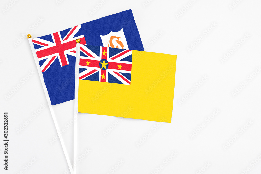 Fototapeta premium Niue and Anguilla stick flags on white background. High quality fabric, miniature national flag. Peaceful global concept.White floor for copy space.