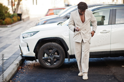 Stylish afro man in beige old school suit against modern hybrid electro suv car. Fashionable young African male in casual jacket on bare torso. © AS Photo Family