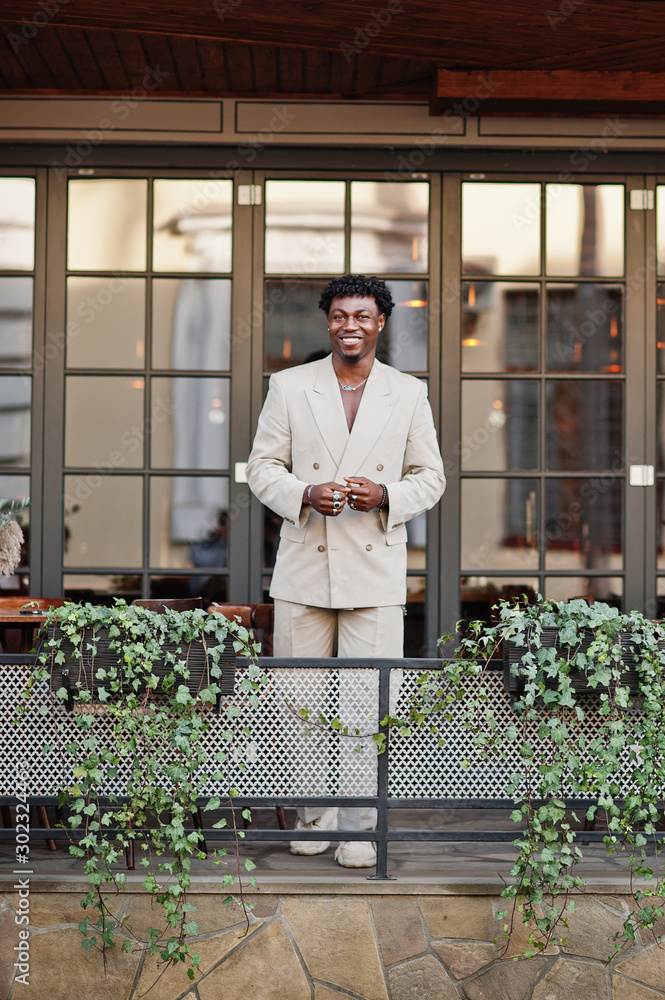 Stylish afro man in beige old school suit standing on terrace of cafe.  Fashionable young African male in casual jacket on bare torso. foto de  Stock | Adobe Stock