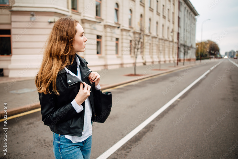 young lovely girl in leather jacket in jeans and with bag is resting outdoors, portrait of woman with beautiful hair in the city young lovely girl in leather jacket in jeans and with bag is resting outdoors, portrait of woman with beautiful hair in the city