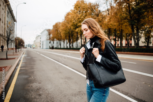 young lovely girl in leather jacket in jeans and with bag is resting outdoors, portrait of woman with beautiful hair in the city © Pavel