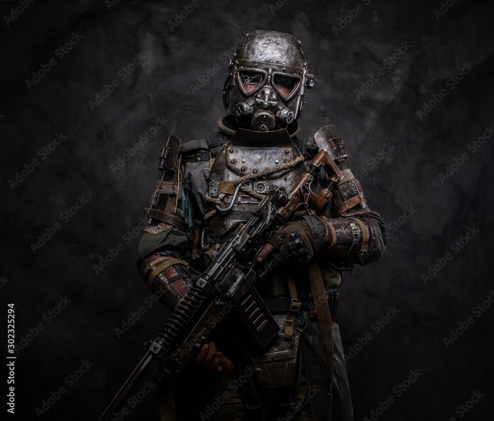Concept of post - apocalypse futuristic warrior with weapon in hands at dark photo studio.