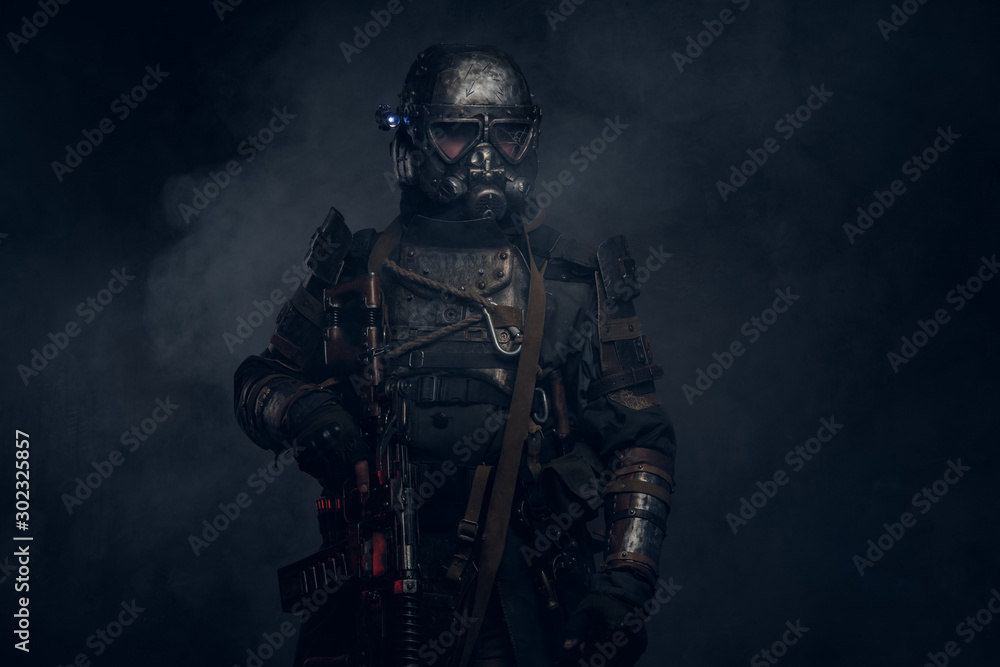 Fototapeta premium In the mist of smoke at dark studio man in dark apocalypse knight costume is posing for photographer.