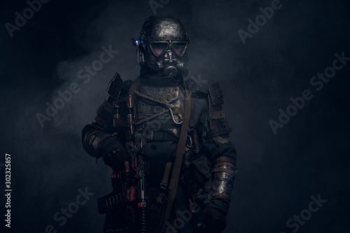 In the mist of smoke at dark studio man in dark apocalypse knight costume is posing for photographer.