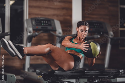 Slim dark-haired girl dressed in sports clothes doing exercises for the press on the mat for fitness with fitness ball in the gym