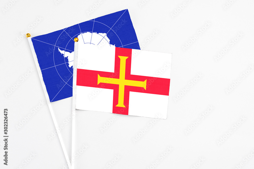 Guernsey and Antarctica stick flags on white background. High quality fabric, miniature national flag. Peaceful global concept.White floor for copy space.