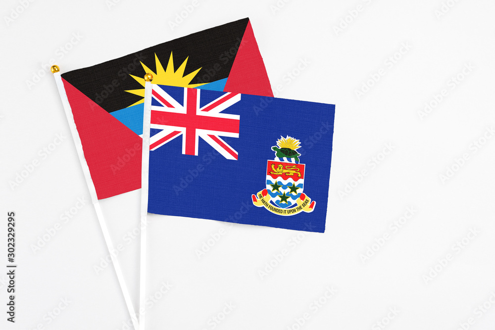 Fototapeta premium Cayman Islands and Antigua and Barbuda stick flags on white background. High quality fabric, miniature national flag. Peaceful global concept.White floor for copy space.