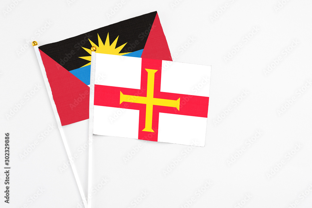 Fototapeta premium Guernsey and Antigua and Barbuda stick flags on white background. High quality fabric, miniature national flag. Peaceful global concept.White floor for copy space.
