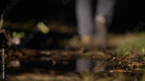 Mysterious man walks into the distance into the dark, stepping into the mud and puddle, close-up of shoes and legs