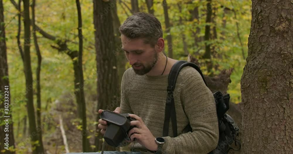 Male Caucasian tourist sitting in the autumn forest with his camera and talking. Confident gray-haired handsome man spending free time outdoors. Cinema 4k footage ProRes HQ. Male Caucasian tourist sitting in the autumn forest with his camera and talking. Confident gray-haired handsome man spending free time outdoors. Cinema 4k footage ProRes HQ.