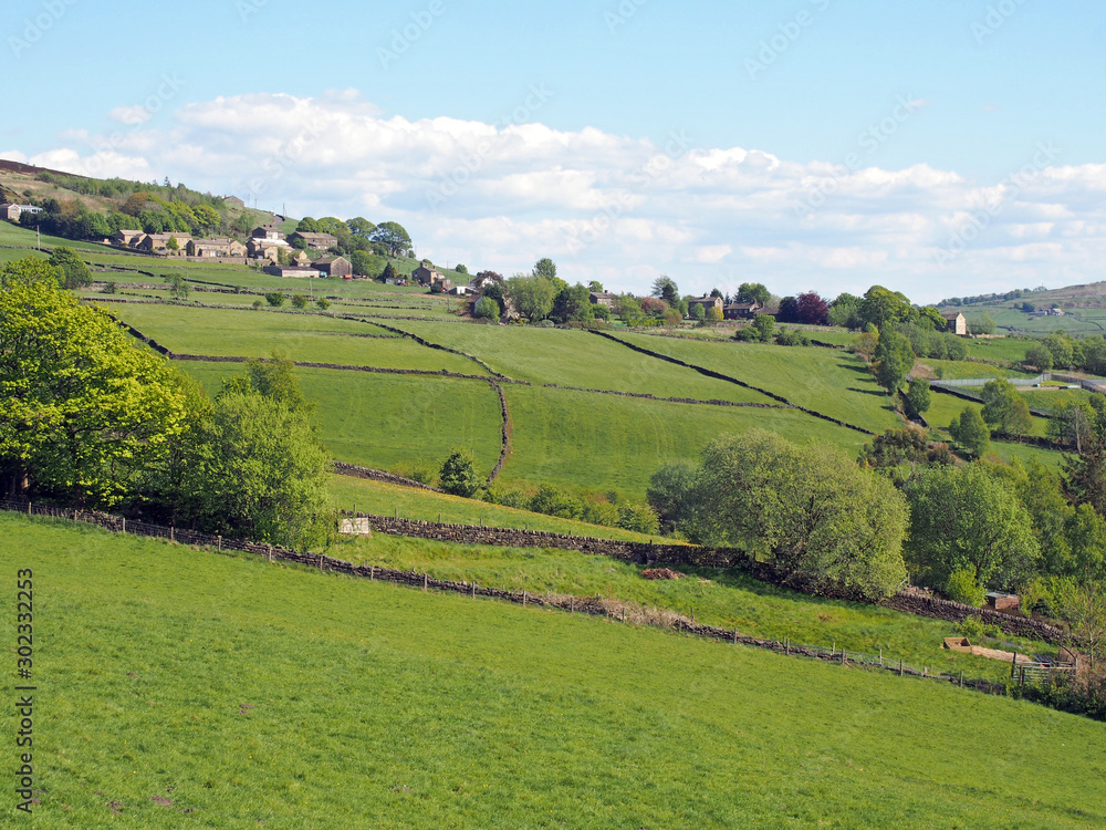 Fototapeta premium sunlit spring countryside with hillside fields and stone walls with the village of old town in calderdale west yorkshire