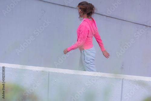 Fototapeta Naklejka Na Ścianę i Meble -  Young female runner in hoody jogging in the city street.Fit body requires hard work. Urban sport concept. Young female exercising in sport clothes.