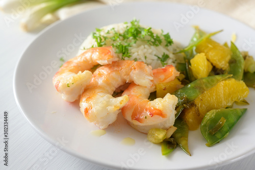 fried tiger prawn shrimp dish with sugar peas, onion and oranges served with rice and parsley garnish on a white plate, selected focus, narrow depth of field