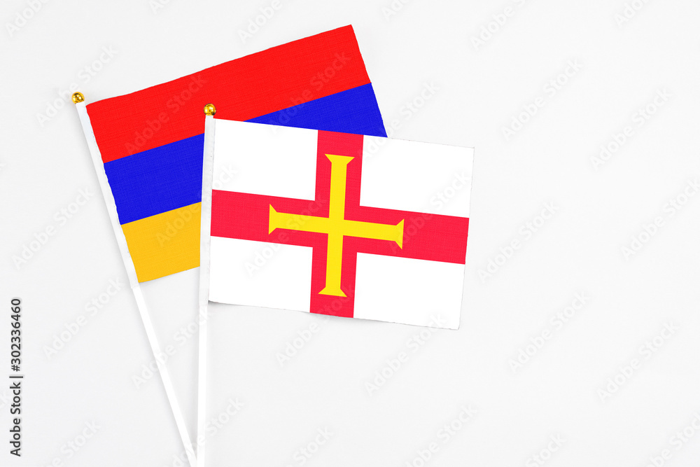 Guernsey and Armenia stick flags on white background. High quality fabric, miniature national flag. Peaceful global concept.White floor for copy space.