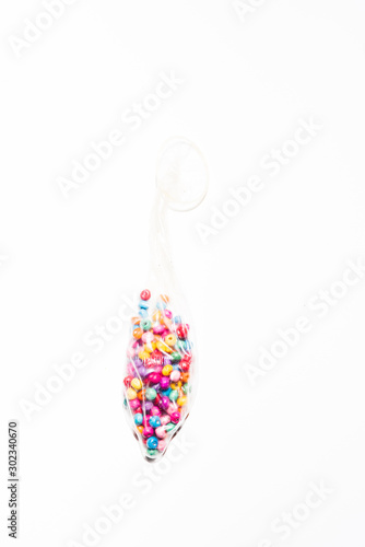 Condom full of colored pearls over a white background, conceptual image for party , love, emotions.