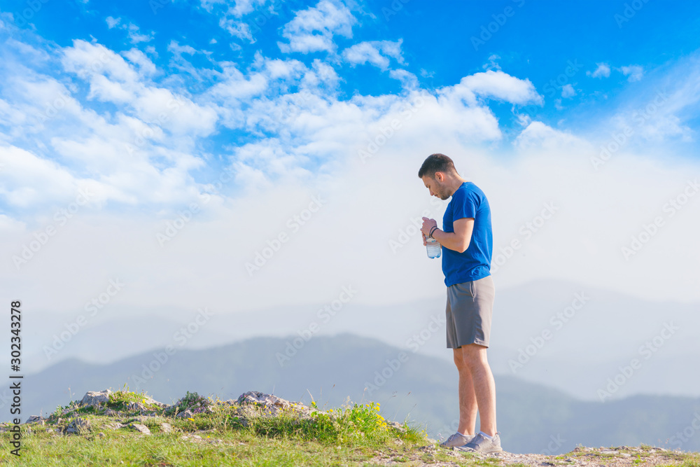 Athlete wearing a blue shirt and grey sports shorts drinks water and prepares for a workout outdoors.