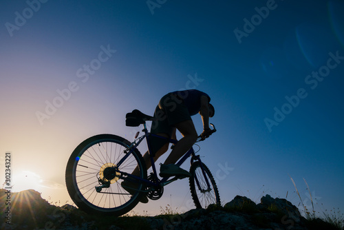 Fototapeta Naklejka Na Ścianę i Meble -  Silhouette of a mountain biker riding his mountain sportbike on top of a cliff ( hill).