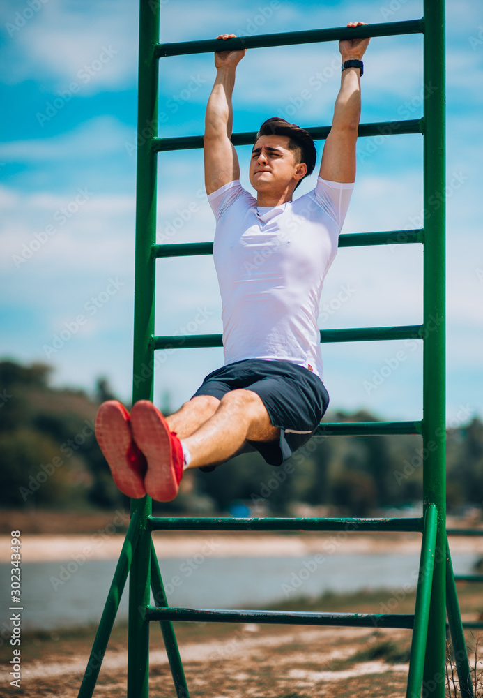 Obraz premium Fit man working out at the beach on chin up bar
