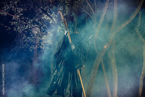 Portrait of grim reaper, the angel of death ( Azrael ) lurking through the woods at night surrounded with mist, smoke in a mystical forest holding his shythe. photo