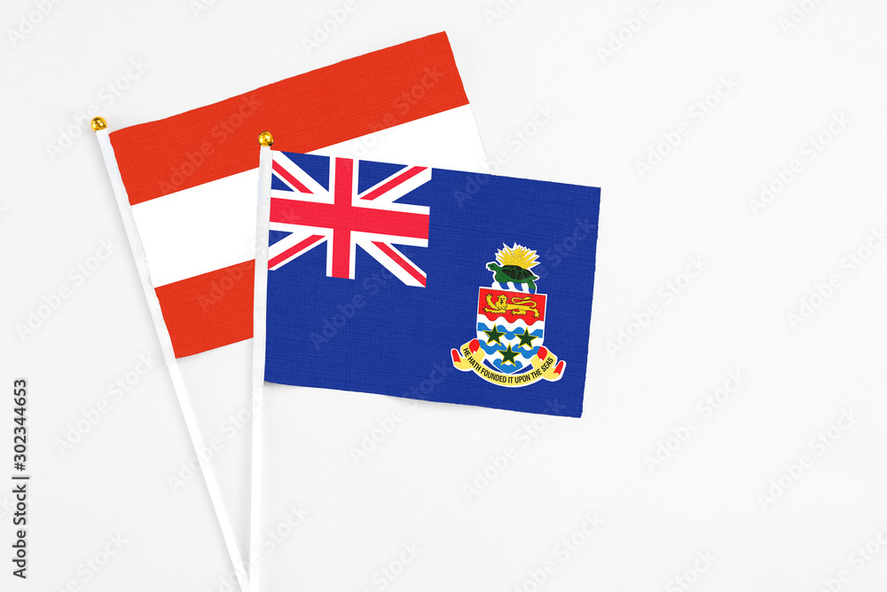 Fototapeta premium Cayman Islands and Austria stick flags on white background. High quality fabric, miniature national flag. Peaceful global concept.White floor for copy space.