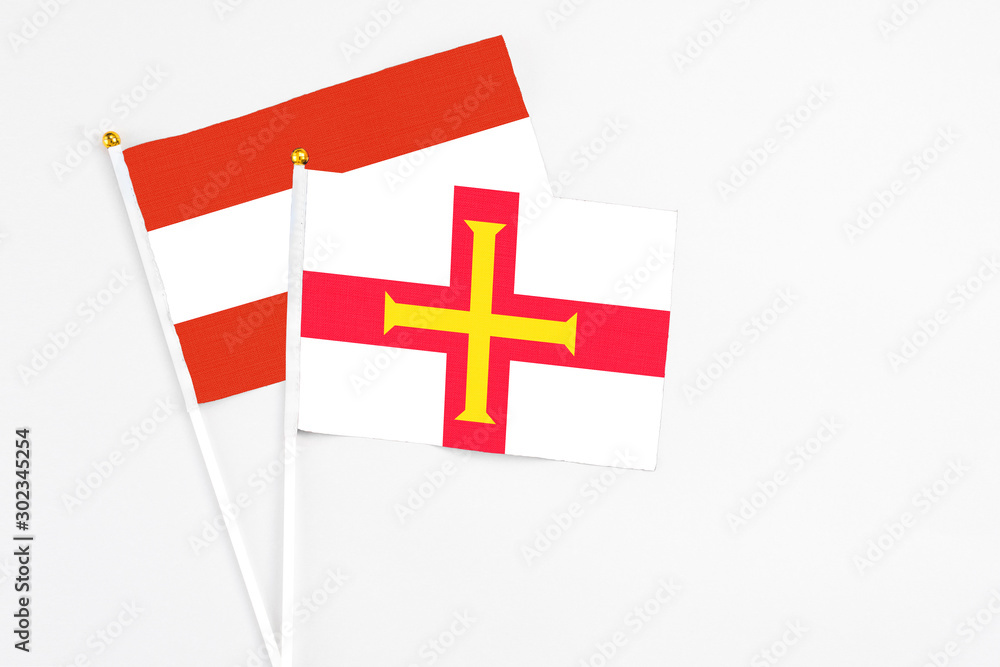 Guernsey and Austria stick flags on white background. High quality fabric, miniature national flag. Peaceful global concept.White floor for copy space.