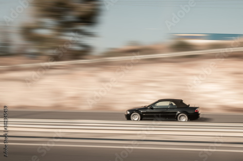 Black car moving fast along the street on a motion blurred background. Car driving on freeway, motion blur. Luxury-car cabriolet.