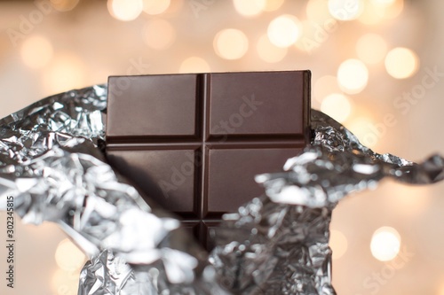 Принти на полотні a bar of a dark chocolate in a silver wrap with gold christmas lights on backgro