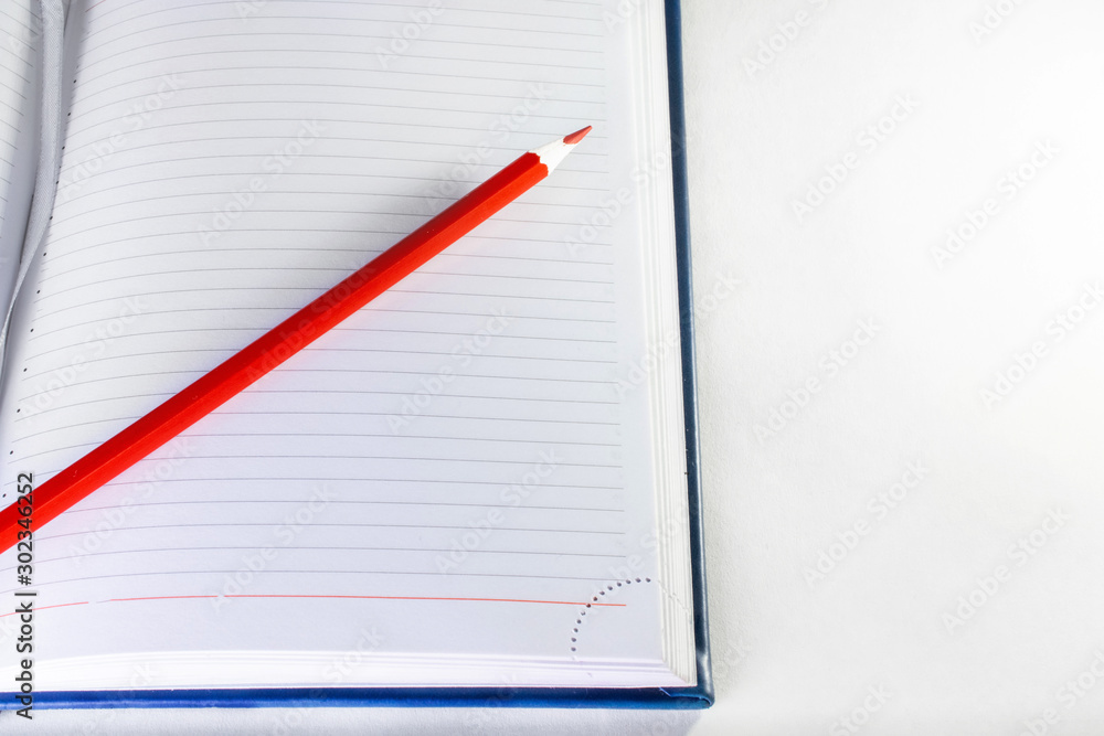 a red pencil on the open notebook on white background a red pencil on the open notebook on white background