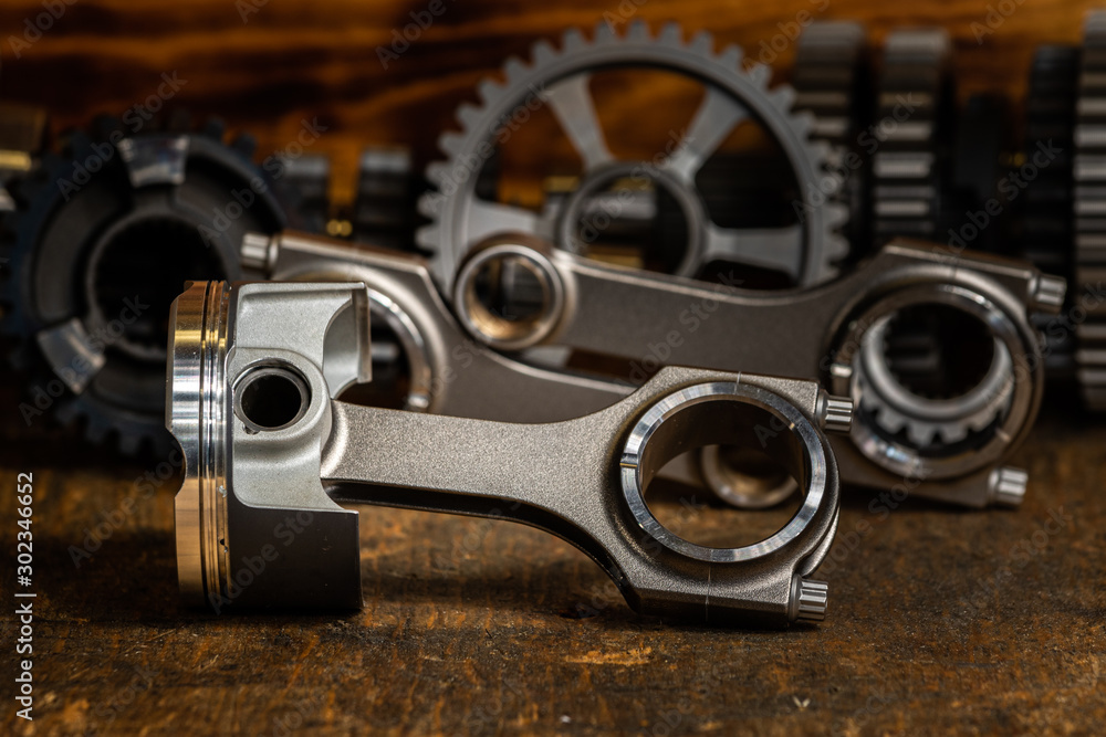 high performance racing motorcycle piston and Conrods on a workbench with gears in the background. high performance racing motorcycle piston and Conrods on a workbench with gears in the background.