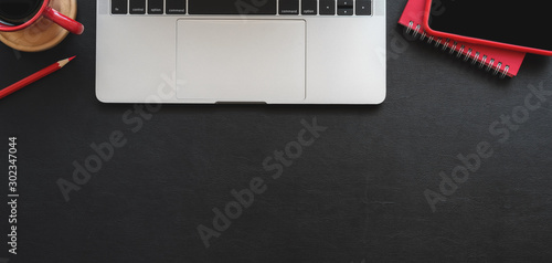 Top view of modern workplace with laptop computer and red office supplies on black table