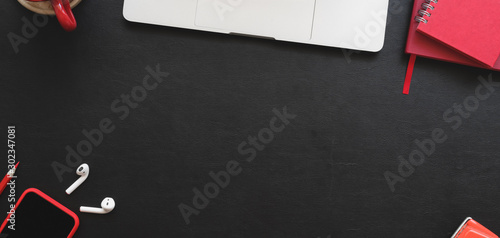 Overhead shot of modern workplace with laptop computer and red office supplies on black table