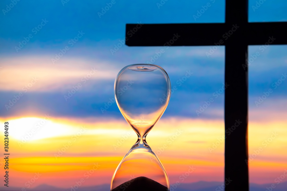 Hourglass has finished counting time on the background of the sunset and a wooden cross. End of life. The value of time in life.. - obrazy, fototapety, plakaty 