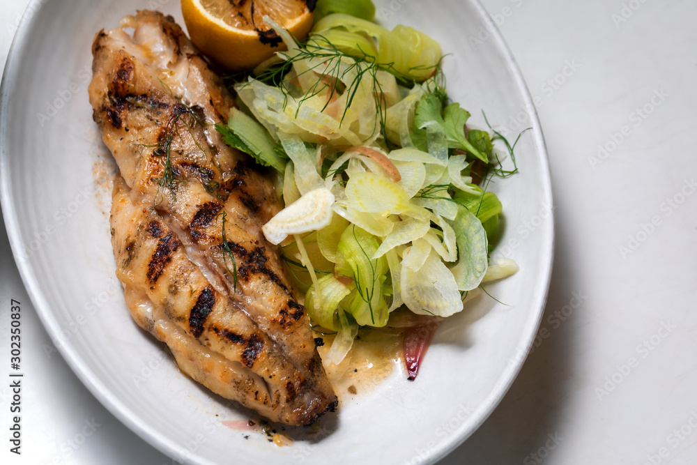 Grilled white fish with lemon and greens on a side outside restaurant interior Grilled white fish with lemon and greens on a side outside restaurant interior