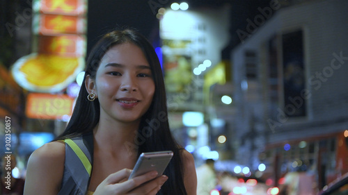 Travel concept. Beautiful girls are playing mobile phones to have fun in the city at night. 4k Resolution.