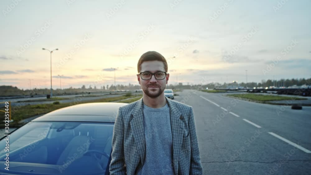 Confident young man in glasses and business suit staying at car in open space outside. Portrait of satisfied successful modern guy. Confident young man in glasses and business suit staying at car in open space outside. Portrait of satisfied successful modern guy.